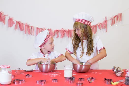 happy smiling children in apron and chef hat cooking cookies with flour, eggs, chocolate and water. Kitchen and family. Happy kids.