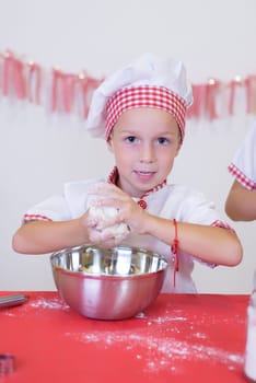 Toddler boy playing with the dough in the kitchen dressed as a chef. Child baking a cake.