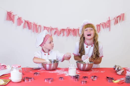 happy smiling children in apron and chef hat cooking cookies with flour, eggs, chocolate and water. Kitchen and family. Happy kids.