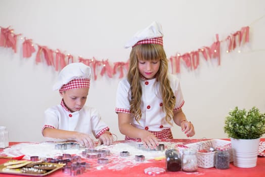 happy smiling children in apron and chef hat cooking cookies with flour, eggs, chocolate and water. Kitchen and family. Happy kids.