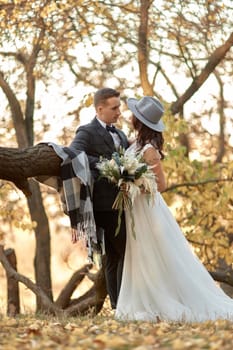beautiful happy stylish bride in hat and groom hugging outdoor in autumn