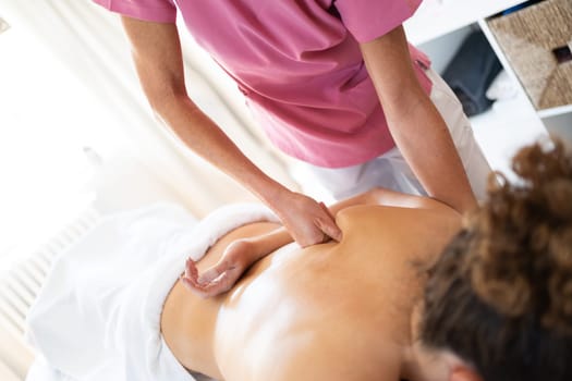 Crop high angle of anonymous osteopath using fist on shoulder bone at back of patient lying face down during physiotherapy session in modern clinic