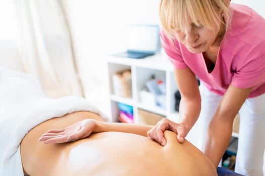 Crop topless unrecognizable female lying face down and receiving osteopathic massage on shoulder blade during rehabilitation session in modern clinic