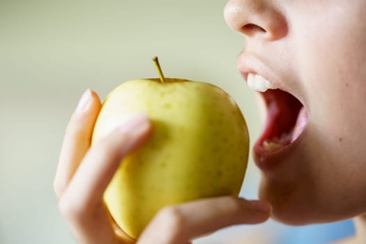 Crop unrecognizable teenage girl with mouth open about to eat fresh yellow apple at home