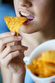 Crop anonymous young girl with mouth wide open about to eat delicious Mexican tortilla chip at home