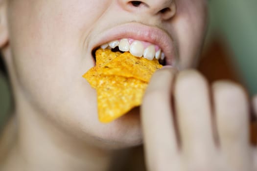 Closeup of crop anonymous young girl biting yummy crunchy Mexican tortilla chips at home