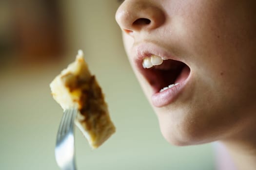 Closeup of crop unrecognizable teenage girl with mouth open about to eat yummy potato omelette from fork at home