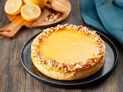 Vegan lemon tart or lemon cake, modernly decorated chopped walnuts. Delicious whole lemon pie on plate on wooden background. Aesthetic of traditional classic french yellow tart with lemon curd recipe