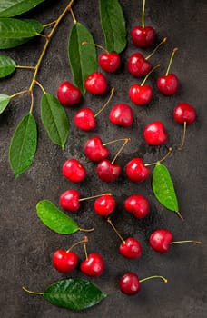 Ripe sweet cherry berry with leaves on a black wooden board.