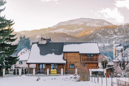 Two-story wooden cottage in a snowy village at the foot of the mountains. High quality photo