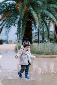 Little girl in rubber boots walks in a puddle in the park. High quality photo