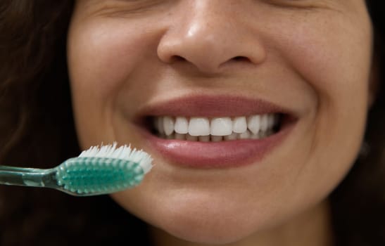 Extreme close-up of beautiful smile of a happy woman with clean white teeth, holding a toothbrush near her mouth, brushing teeth with toothpaste. Dental care and oral hygiene. Teeth whitening concept