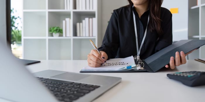 Charming Asian business woman sitting working on laptop in office.