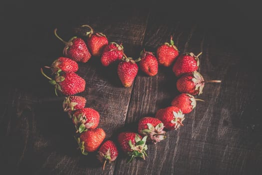 Ripe strawberry fruit. Strawberries in the shape of heart. Strawberries on a wooden background. Healthy food. Organic food. Fruit on a wooden table. Sweet dessert of fruit.