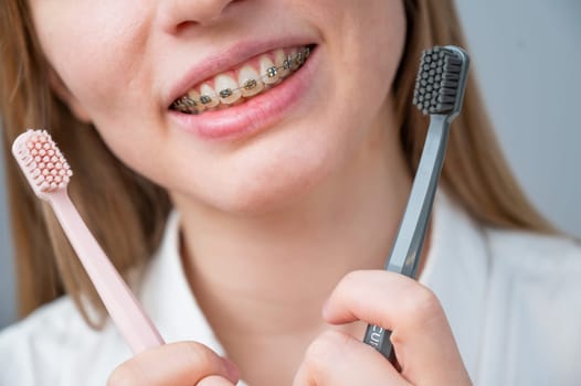 Cropped portrait of young smiling woman with braces holding two toothbrushes