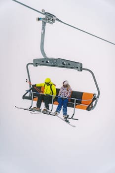 Skiers in colorful ski suits on skis riding on a chairlift up the mountain. High quality photo