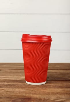 Close up big red paper coffee or tea cup on brown wooden table over white painted wall at coffee shop retail display