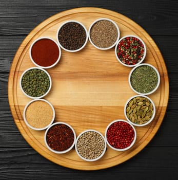 Round frame of assorted spices in white ceramic bowls over dark wooden table background with copy space, elevated top view, directly above