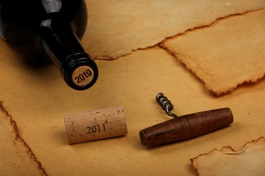 Close up one full unopen bottle of red wine with cork and retro opener with wooden handle over vintage brown paper background with copy space, high angle view