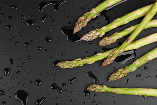Close up bunch of washed fresh green asparagus on black table with drops of water, elevated top view, directly above