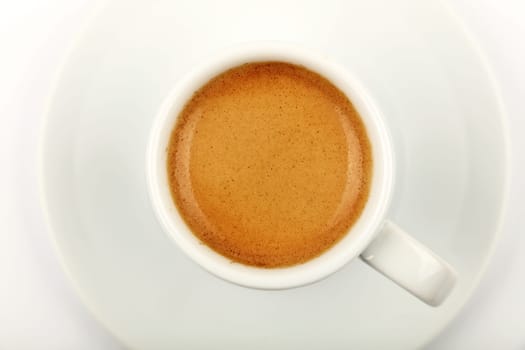 White cup full of espresso coffee with brown crema, on saucer, on white background, elevated top view, directly above