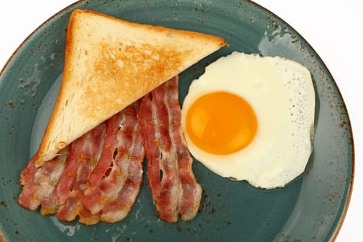 Close up English breakfast, sunny side egg, toasted bread and roasted bacon slices on blue plate isolated on white background, high angle view