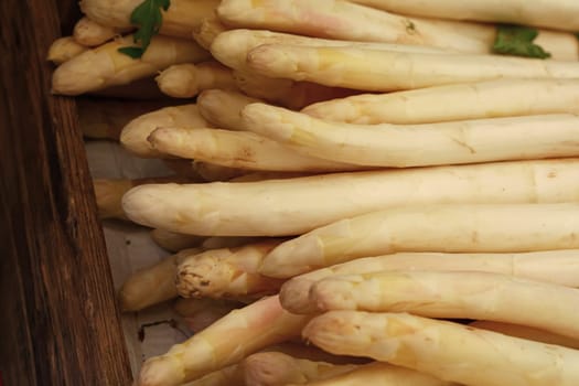 Close up fresh white asparagus in wooden box at retail display of farmer market, high angle view
