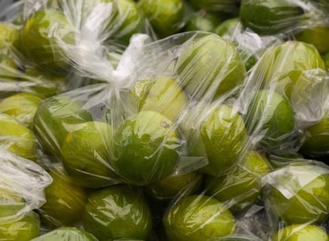 Close up green lime fruits in plastic bag on retail display of farmer market, high angle view