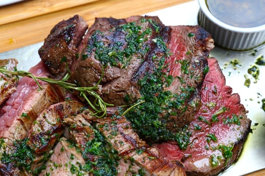 Close up big portion of sliced grill roasted beef chateaubriand tenderloin meat with thyme and herbs served on wooden cutting board, high angle view