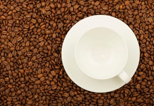 Close up empty white cup on saucer over background of roasted coffee beans, elevated top view, directly above