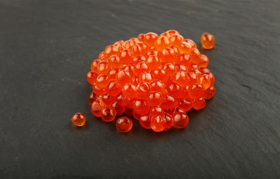 Close up one heap portion of salmon fish red caviar on background of black slate kitchen board, high angle view
