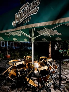 Red cat sits on a street bar table under an umbrella at night. High quality photo