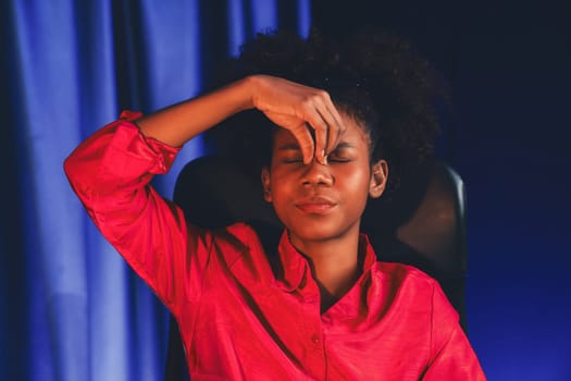 African woman businesswoman, wearing pink shirt having headache with migraine, sitting at computer laptop with leaning position. Concept of work form home with pressure and tension. Tastemaker.