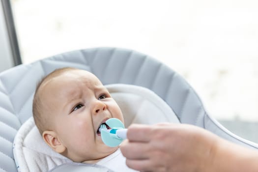 Newborn baby suffering of his tooth growth, mom using teether to ease the pain, healthcare concept