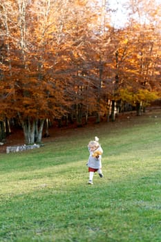 Little girl with a bouquet of autumn leaves runs through a green meadow. High quality photo