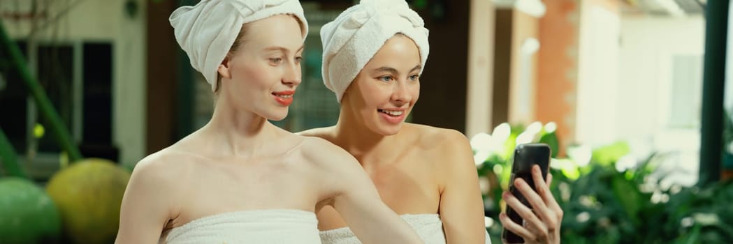 Couple of young beautiful women with beautiful skin in white towel taking a photo together at outdoor surrounded by peaceful natural environment. Beauty and healthy spa concept. Tranquility.