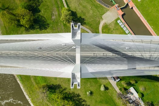 Famous cable-stayed Redzinski Bridge over blue flowing river among lush green forests. Scenic nature and urban infrastructure near Wroclaw aerial view