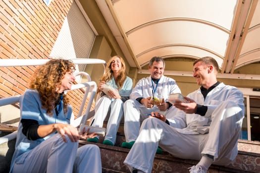 Happy doctors and nurses sharing lunch time outside the hospital in a sunny day