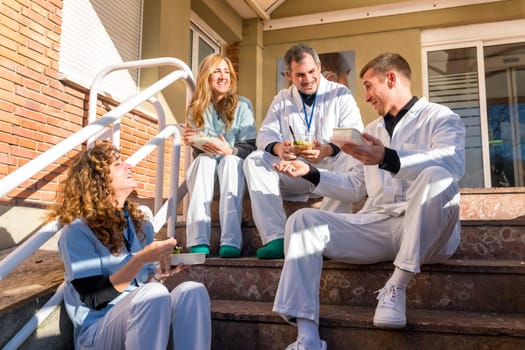 Medical coworkers smiling and chatting during lunch time sitting on stairs outdoors