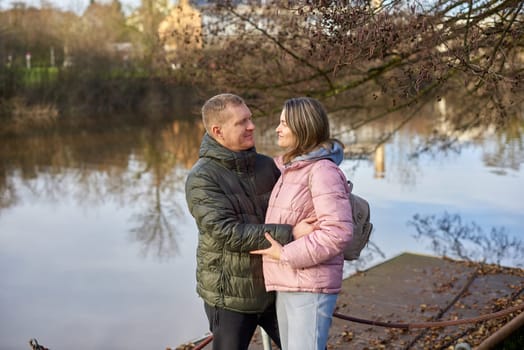 Loving couple sit on the shore of the pond in the park in autumn. A man and a woman. A couple, lovers on the shore of the lake on a walk