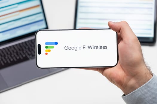 Google Fi Wireless logo of app on the screen of mobile phone held by man in front of the laptop and tablet, December 2023, Prague, Czech Republic
