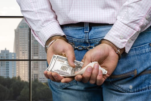 Close up male hands in handcuffs holding money. Crime and bribery concept.