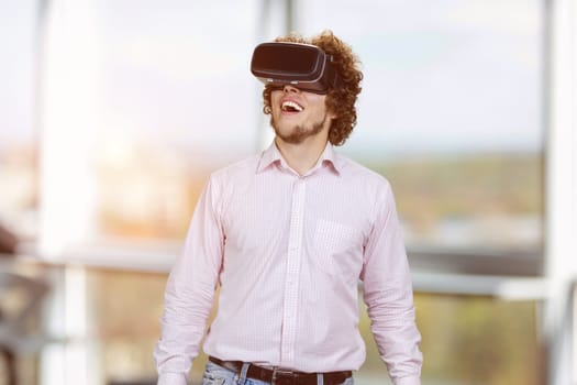 Portrait of young happy man with curly hair wearing vr headset. Indoor window in the background.