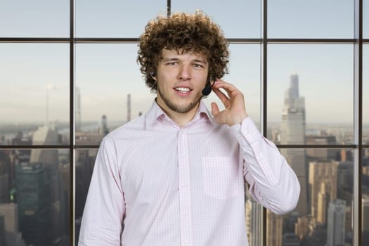 Portrait of a happy young successful man talking in microphone touching in with finger. Checkered window with cityscape view in the background.