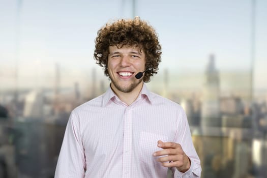 Happy cheerful successful man wearing microphone laughing. Blurred cityscape in the background.
