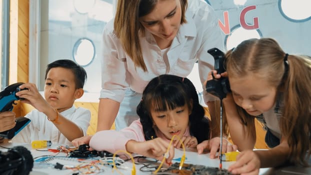 Teacher looking at children while diverse student looking at screen. Children excited in presentation while drawing or writing art books at table with toys and color pencil placed on table. Erudition.