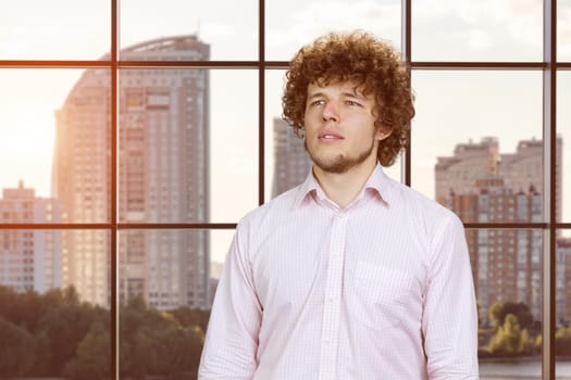 Portrait of a happy young attractive man with curly hair. Checkered indoor window in the background.