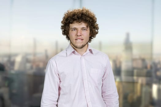 Portrait of happy of a young attractive man with curly hair bites his lip. Blurred urban scape in the background.