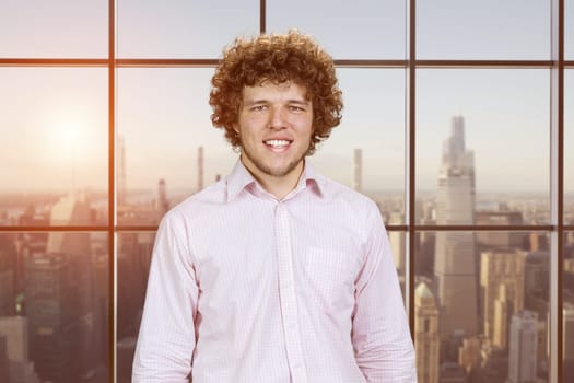 Portrait of a happy young smiling man with curly hair. Checkered window with cityscape view.
