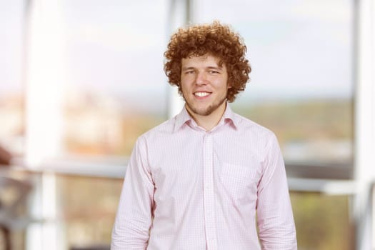 Portrait of a happy young cheerful man with curly hair. Indoor window in the background.